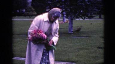 1968: elderly woman carrying flowers in graveyard searching for something