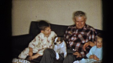 1968: two young lads and elderly couple with pet seated on couch hugging