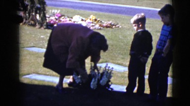 1968: Two Boys Quietly Watch as a Woman Straightens a Bouquet of Flowers at a Tombstone