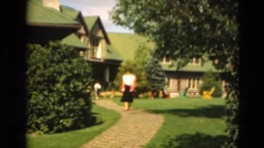 1949: a dark haired woman in a black skirt strolls through a yard