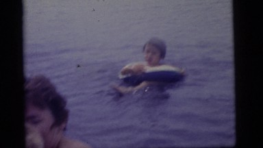 1965: a little boy clings to his mother in the water while his brother swims