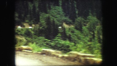 1967: driving behind camper on road with pine trees and rock barriers SOUTH