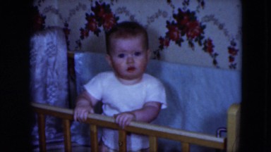 1951: baby stands in crib holding railing and showing emotions while moving