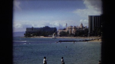 1967: tourists moving about on a beautiful ocean beach with palm trees HAWAII