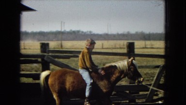 1967: a man holding a rope as a young boy learns to ride a horse behind him