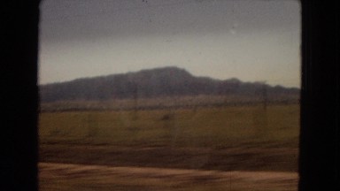 1967: a vehicle is moving on the road along a vast field edged by mountains