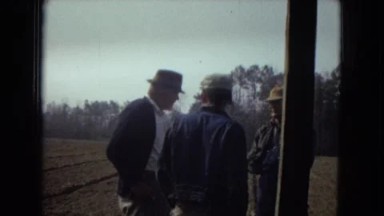 1967: a man in a jacket and hat talking to two men while standing in a field