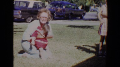 1967: woman holding a baby girl in a red dress and helping her stand up. TUCSON
