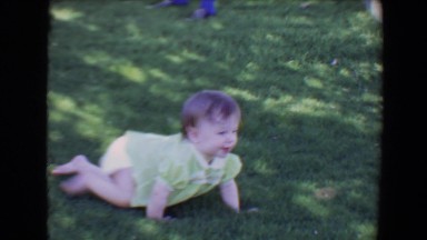 1967: baby smiling crawling in grass towards cinder block fence TUCSON, ARIZONA