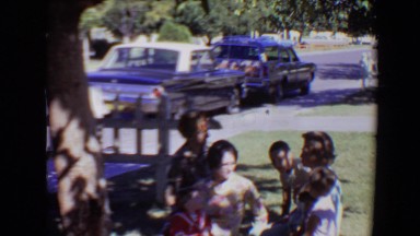 1967: a gathering in the yard shows a little girl in a red dress and people