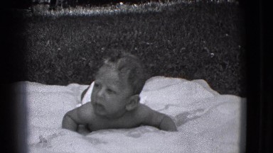 1941: Little Boy Raising Head Posing While Lying on White Blanket