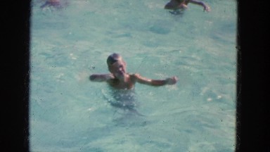 1965: young man swimming past girls in a clear blue public pool CALIFORNIA