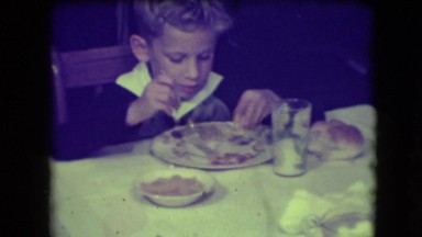 1946: Boy at Dinner Table Eating, Smiling and Laughing at Camera