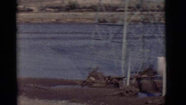 1964: sand water people walking boat on shore windy grey logs cell tower