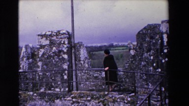 1969: an old woman in black coat walking on a stony structure IRELAND