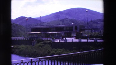 1969: a building and mountains as seen across the water on a bridge LOURDES