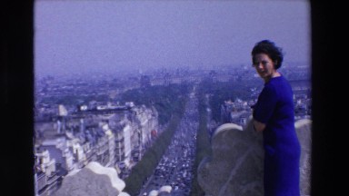1969: a smiling woman in blue dress on a balcony overlooking city LOURDES