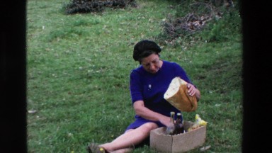 1969: A Woman Cutting a Huge Piece of Bread Sitting on Grass Lourdes, France