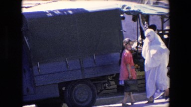 1971: a woman in a burka walking past military vehicles