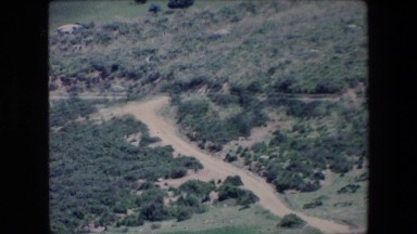 1971: small dust covered path leads to a tree covered mountain peak