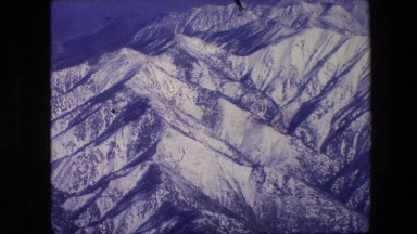 1967: an aerial view of snow capped mountain ranges in the summer from a plane