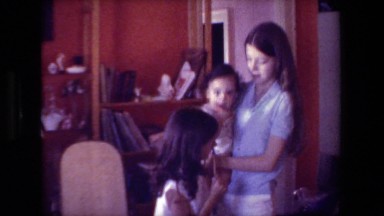 1981: two girls playing with baby in home with bookcase in background HOLLYWOOD