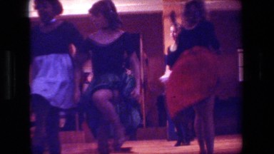 1981: girls in period costumes do a line dance on a stage for an audience