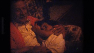 1981: baby sleeping grandfathers lap girl sitting opening box sandals LANSING