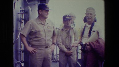 1981: group of personnel smile and chat casually while aboard a naval vessel.