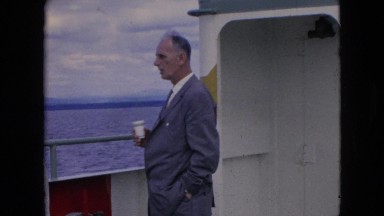 1964: man standing on the deck of a ferry, drinking from a paper cup