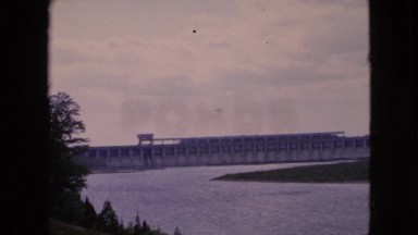 1964: large reservoir of a dam with islands of grass under the clear sky