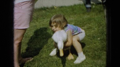 1965: Little Girl Picks Up and Carries White Duck on Lawn in Wellsburg, Iowa
