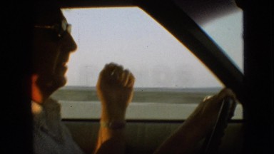 1968: an old man wearing specs driving a car through a vast field MISSOURI
