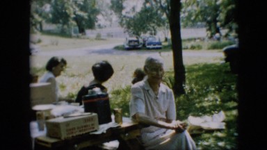 1957: a group of old and young people sitting in a park at a gathering with food