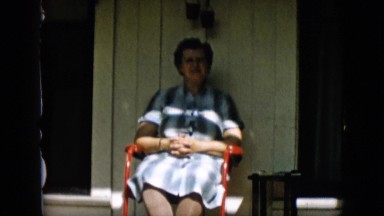 1957: woman sitting outside on a porch, swinging her feet and waving.