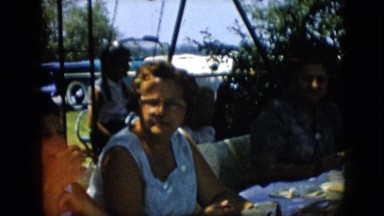 1957: elderly woman sitting at a table with kids in the background playing