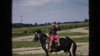 1957: cute girl sitting on black horse with tail field calling someone beautiful