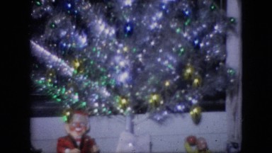 1964: Man Sitting on Sofa Smiling at Christmas Tree with Lights and Toys