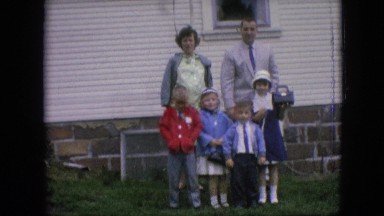 1964: father waves gestures at cameraperson while mother and four children stand
