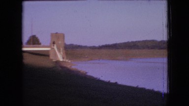 1964: a calm beautiful lake with shore rich in greenery and a boat moves through
