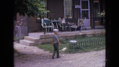 1964: cute kid with hat walking along fence of a house PHILADELPHIA PENNSYLVANIA