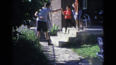 1965: father standing children playing boxing hand house trees greenery around
