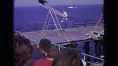 1966: acrobat show on dock of two people on a seesaw like structure, and a woman