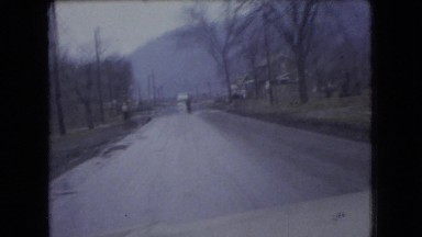 1966: car drives speedily toward man standing with arm extended on rural road