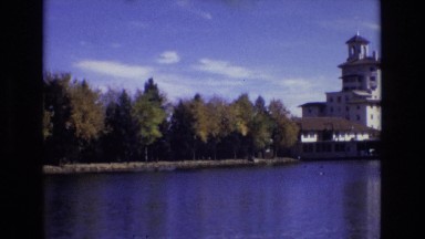 1967: a large building sits on the banks of a lake next to a line of trees