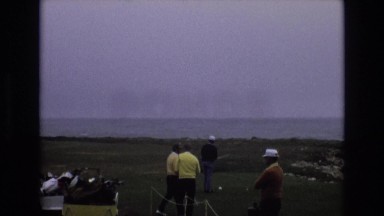 1965: golf buddies standing on the green looking out over the ocean CENTRAL
