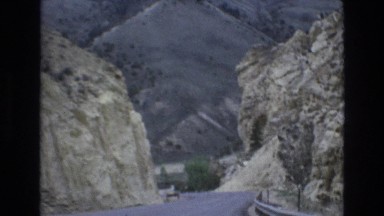 1965: a road or highway cutting through the mountains as seen from a vehicle