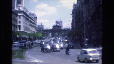 1969: on a busy roads cars moving to and fro surrounded by tall buildings SPAIN