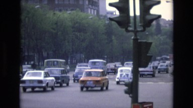 1969: cars moving on road trees around traffic signal people rushing buildings