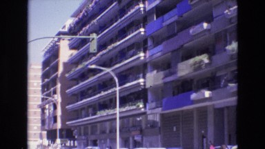 1969: Street Lights in Front of Buildings with Cars Driving Below in Spain